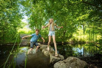 Kinderen spelen op stenen in het water in de natuurspeeltuin op Landal Klein Oisterwijk