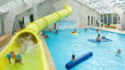 Mensen in het binnenbad met grote gele glijbaan van vakantiepark Molecaten Park Wijde Blick