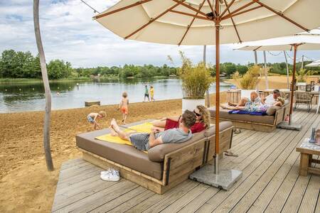 Mensen op loungestoelen op het terras van de Beachbar op vakantiepark BreeBronne