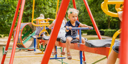 Kinderen op de familieschommel in een speeltuin op vakantiepark BreeBronne