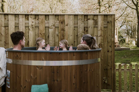 Een gezin zit in de hottub in de tuin van een bungalow op vakantiepark Dierenbos