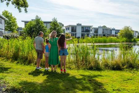 Gezin kijkt over het water naar vakantiehuizen op vakantiepark EuroParcs Bad Hulckesteijn