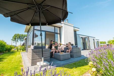 Een gezin op een loungeset in de tuin van een vakantiehuis op vakantiepark EuroParcs Bad MeerSee