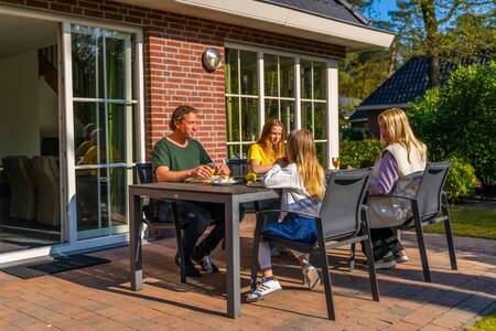 Gezin aan tafel in de tuin van een vakantiehuis op vakantiepark EuroParcs Beekbergen