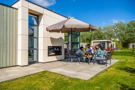 Gezin aan tafel in de tuin van een vakantiehuis op vakantiepark EuroParcs Buitenhuizen