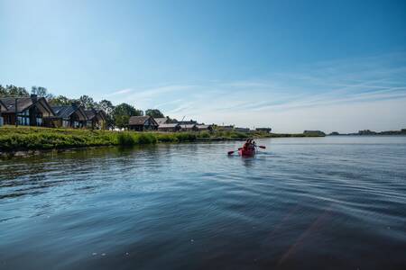 Mensen aan het kanovaren langs vakantiehuizen op vakantiepark EuroParcs De IJssel Eilanden