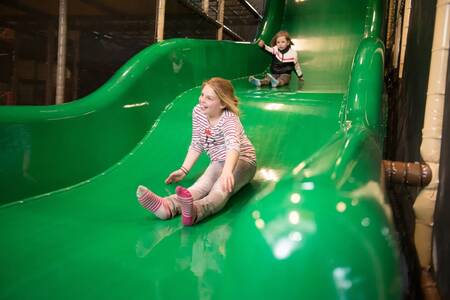 Kinderen op de glijbaan in de Indoor speeltuin van vakantiepark EuroParcs De Wije Werelt