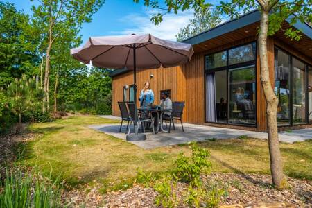 Gezin aan tafel in de tuin van een vakantiehuis op vakantiepark EuroParcs De Wije Werelt