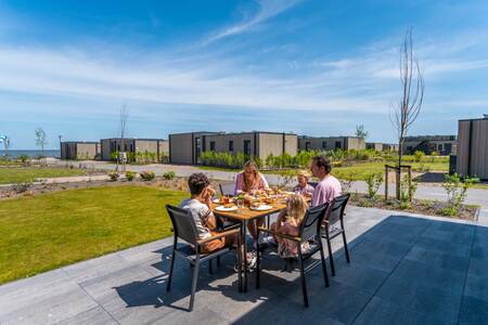 Gezin aan een tafel in de tuin van een vakantiehuis op vakantiepark EuroParcs Enkhuizer Strand