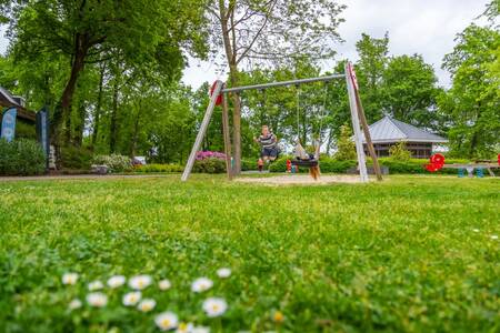 Kinderen op de schommel in een speeltuin op vakantiepark EuroParcs Maasduinen