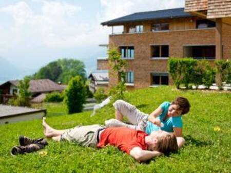 2 personen liggen op het gras voor een appartementencomplex op Landal Alpen Chalet Matin
