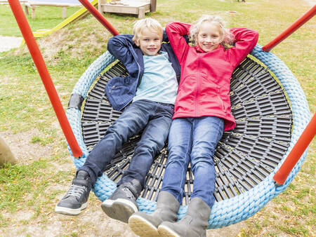 2 kinderen op een schommel in een speeltuin op vakantiepark Landal Hochwald