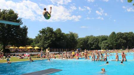 Jongen springt van de duikplank in het buitenbad van vakantiepark Molecaten Bosbad Hoeven