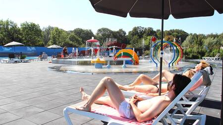 Mensen op ligstoelen bij het buitenzwembad van Molecaten Park Rondeweibos