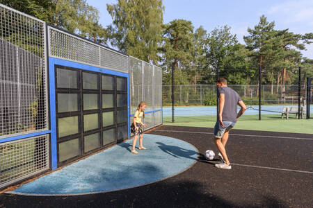 Vader en dochter voetballen op het speelveld op vakantiepark RCN het Grote Bos