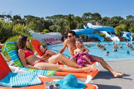 Gezin op ligstoelen naast het buitenbad van vakantiepark Roompot Le Littoral