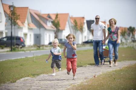 Gezin wandelt langs vakantiehuizen op vakantiepark Roompot Noordzee Résidence Cadzand-Bad