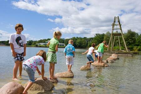 Kinderen spelen op stenen in het recreatiemeer van Roompot Vakantiepark Hunzedal