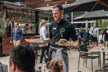 Een ober brengt een diner op het terras van Roompot Vakantiepark Kijkduin