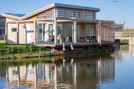 Mensen op het terras direct aan het water van een vakantiehuis op vakantiepark Roompot Water Village