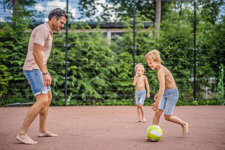 Vader met kinderen aan het voetballen op het voetbalveld