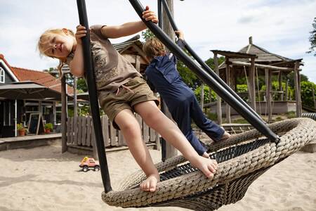 Kinderen op een schommel in een speeltuin op vakantiepark Sandberghe